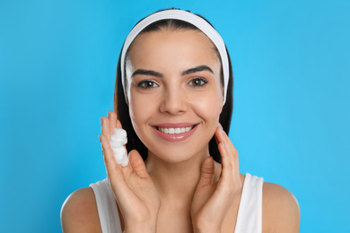 Photo of Young woman applying cosmetic product on light blue background. Washing routine