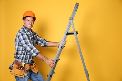 Professional builder climbing up metal ladder on yellow background