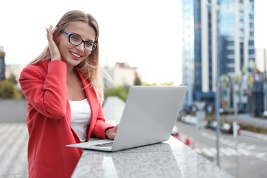 Beautiful businesswoman with glasses using laptop in city