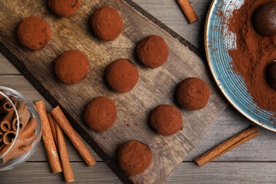 Delicious chocolate truffles with cocoa powder and cinnamon on wooden table, flat lay