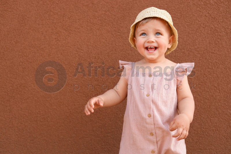 Cute little girl wearing stylish clothes near brown wall. Space for text