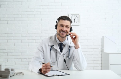 Doctor with headset sitting at desk in clinic. Health service hotline