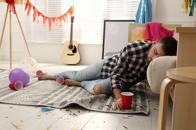 Young man sleeping near sofa in messy room after party