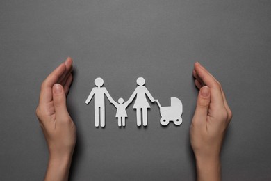 Woman protecting paper family figures on grey background, top view. Insurance concept