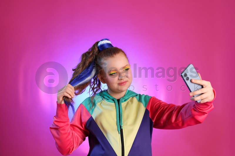 Cute indie girl with smartphone taking selfie on violet background