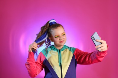Cute indie girl with smartphone taking selfie on violet background
