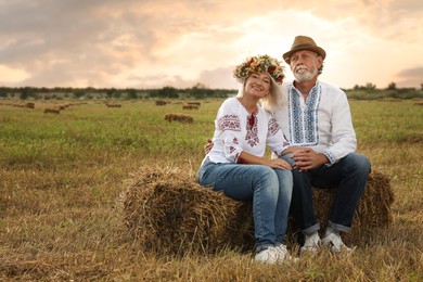Happy mature couple wearing Ukrainian national clothes on hay bale in field