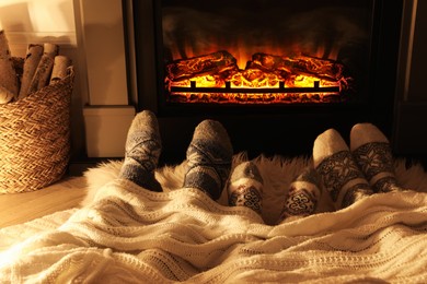 Family in warm socks resting near fireplace at home, closeup of legs