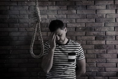 Depressed man near brick wall, focus on rope noose. Suicide concept