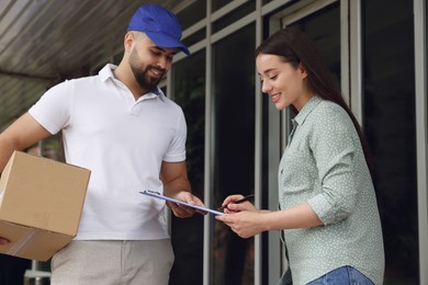 Woman signing for delivered parcel near entrance outdoors