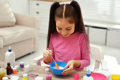 Cute little girl mixing ingredients with silicone spatula at table. DIY slime toy