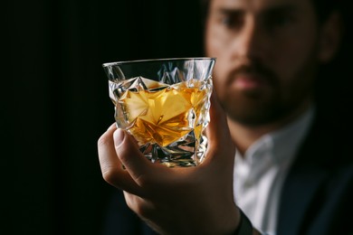 Photo of Man holding glass of whiskey with ice cubes on black background, selective focus