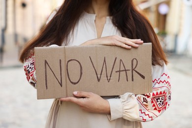 Woman in embroidered dress holding poster No War on city street, closeup
