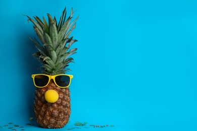 Photo of Pineapple with sunglasses and funny nose on light blue background, space for text. Creative concept