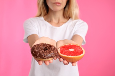 Woman choosing between doughnut and healthy grapefruit on pink background, closeup
