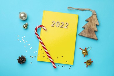 Yellow planner and Christmas decor on light blue background, flat lay. Planning for 2022 New Year