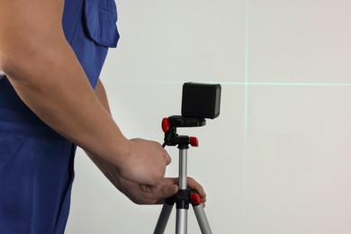 Worker pointing cross line laser level on light wall, closeup