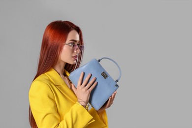 Photo of Stylish woman with red dyed hair and bag on light gray background, space for text