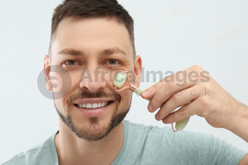 Photo of Man using nephrite facial roller on white background