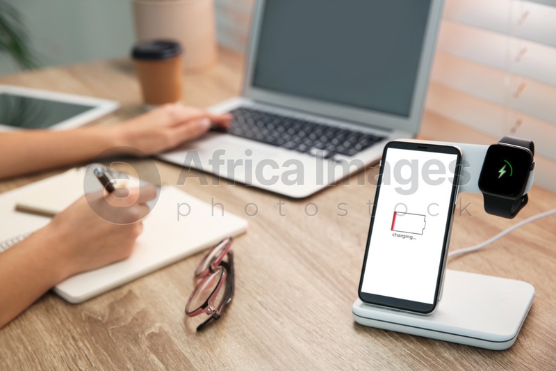 Photo of Woman working at table while her mobile phone charging with wireless device
