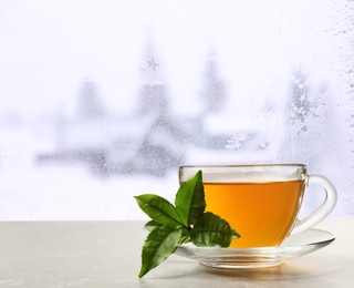 Cup of hot tea on table near window covered with frost 