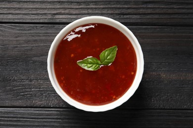 Spicy chili sauce with basil on dark wooden table, top view