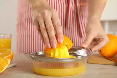 Woman squeezing orange juice at wooden table, closeup