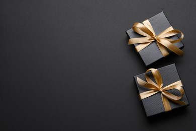 Shiny gift box with golden bow on black background, flat lay. Space for text