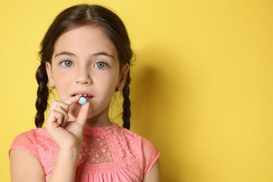 Photo of Little girl taking vitamin pill on yellow background. Space for text