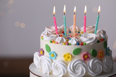 Delicious birthday cake with party decor on stand against blurred festive lights, closeup
