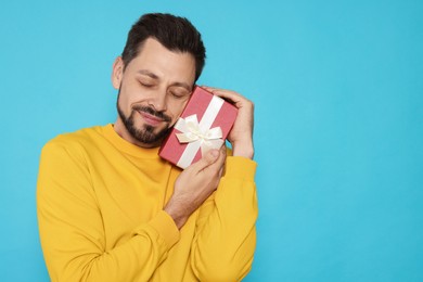 Photo of Happy man with gift box on light blue background, space for text