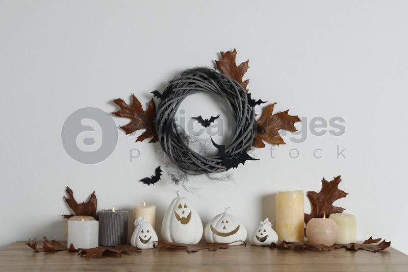 Different pumpkin shaped holders, autumn leaves and burning candles on wooden table. Halloween decor