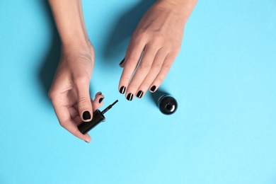Woman applying nail polish with brush on color background, top view
