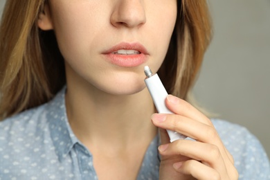 Woman with herpes applying cream onto lip against light grey background, closeup