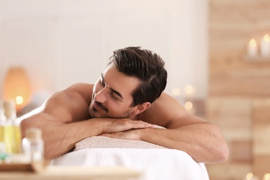 Handsome young man relaxing on massage table in spa salon, space for text