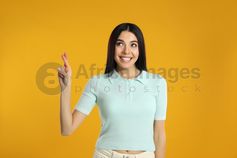 Woman with crossed fingers on yellow background. Superstition concept