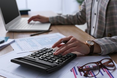 Tax accountant with calculator working at table in office, closeup