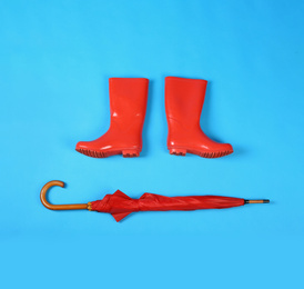 Beautiful red umbrella and rubber boots on blue background, flat lay