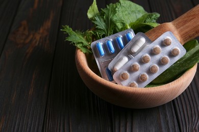 Photo of Mortar with fresh green herbs and pills on wooden table, closeup. Space for text