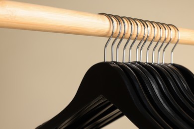 Black clothes hangers on wooden rail against beige background, closeup