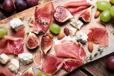 Ripe figs and prosciutto served on wooden table, above view