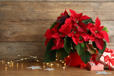 Poinsettia (traditional Christmas flower), string lights and gift boxes on wooden table. Space for text