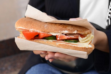 Photo of Woman holding tasty sandwich with vegetables outdoors, closeup. Street food