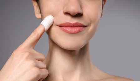 Woman using silkworm cocoon in skin care routine on grey background, closeup