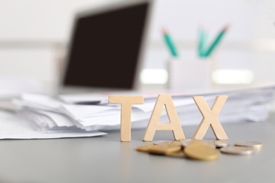 Word TAX and coins on table against blurred background