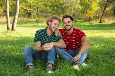 Portrait of happy gay couple sitting on grass in park