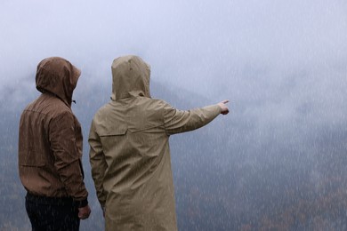 Man and woman in raincoats enjoying mountain landscape under rain
