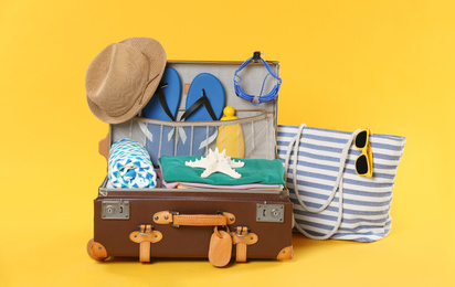 Bag and open vintage suitcase with different beach objects packed for summer vacation on orange background
