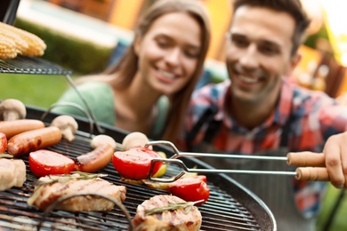 Young man and woman near barbecue grill outdoors, focus on tongs with tomato