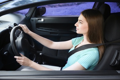 Young woman with fastened safety belt on driver's seat in car